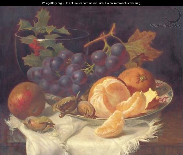 An apple, black grapes, two oranges and cob nuts on oriental plate, with holly in a glass vase, on a wooden table - Eloise Harriet Stannard