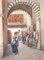 View of a street in a souk with a woman carrying a fruit basket on her head, a carpet stall behind - Vittorio Rappini