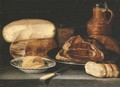 A ham on a pewter dish, a cheesestack, a jug, a glass, butter in a blue and white porcelain dish, bread and a knife on a ledge - (after) Sebastien Stoskopff