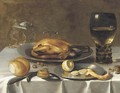 A roemer of wine, a turkey and a partly-peeled lemon on pewter dishes, bread and hazelnuts on a draped table - (after) Pieter Claesz