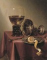 An upturned silver tazza, hazelnuts, a peeled lemon on a pewter platter, a knife and a roemer, on a draped table - Maerten Boelema De Stomme